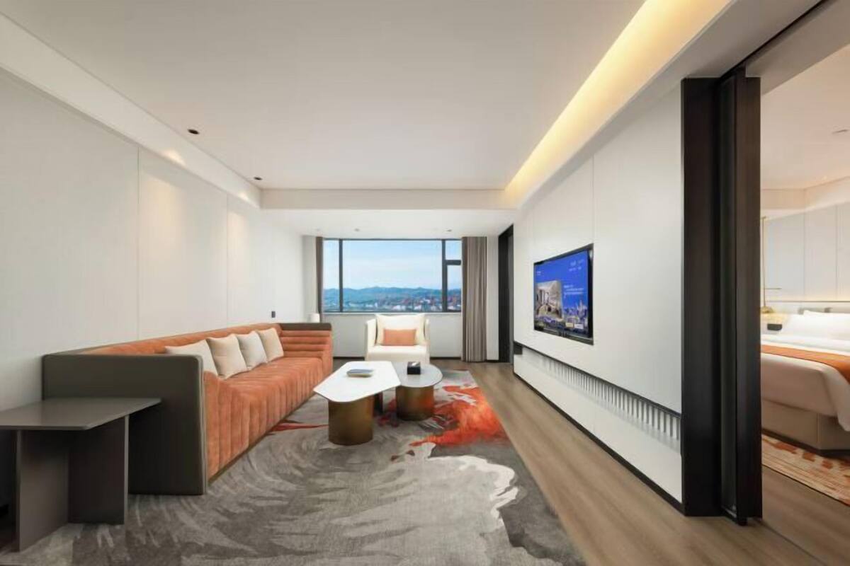A modern hotel room with a sofa, a small table, a TV, and a view of the city.