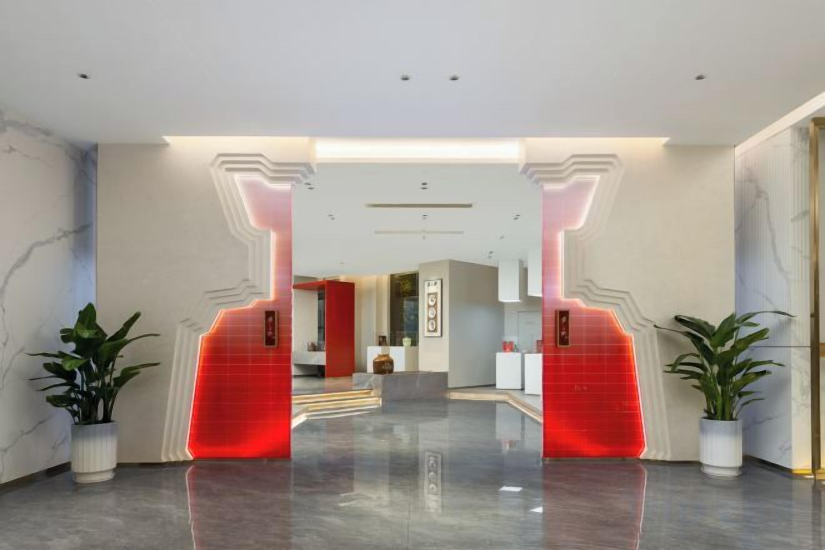 A hotel lobby with a modern design, featuring a reception desk, a staircase, and potted plants.
