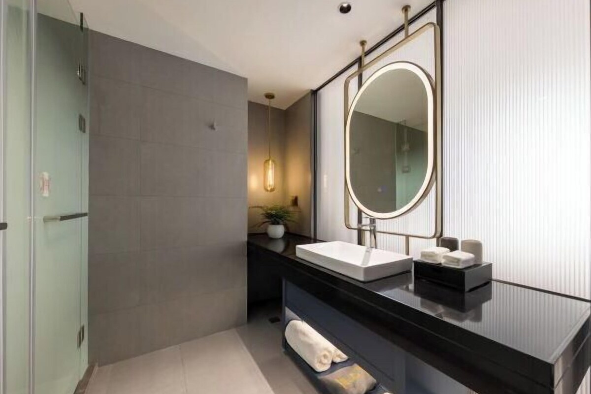 A modern bathroom with a glass shower enclosure, a black vanity with a white sink, and a large mirror.