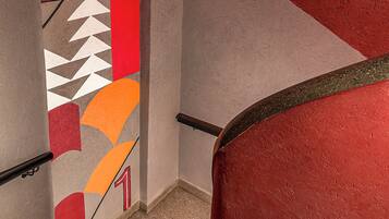 Una escalera con barandilla roja y una pared decorada con patrones geométricos y números.