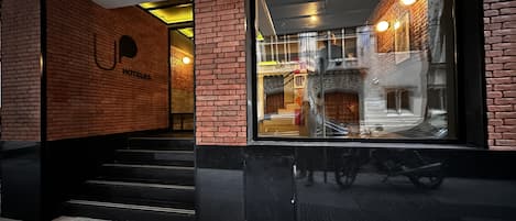 L’entrée d’un hôtel, avec une façade en briques, de grandes fenêtres en verre et un escalier menant à l’intérieur.