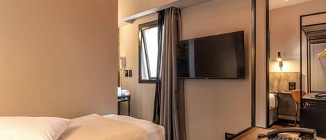 A hotel room with a bed, a TV mounted on the wall, a desk with a chair, and a mirror.