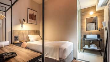 Een hotelkamer met twee bedden, een bureau met telefoon, een lijst met afbeelding en een badkamer met wastafel en spiegel.