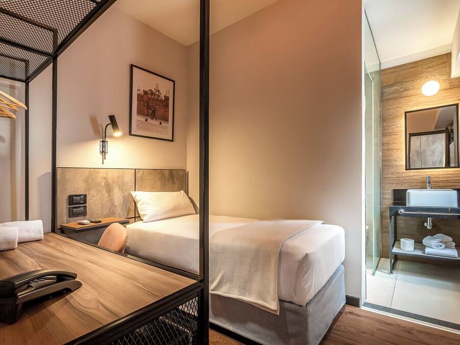 Een hotelkamer met twee bedden, een bureau met telefoon, een lijst met afbeelding en een badkamer met wastafel en spiegel.