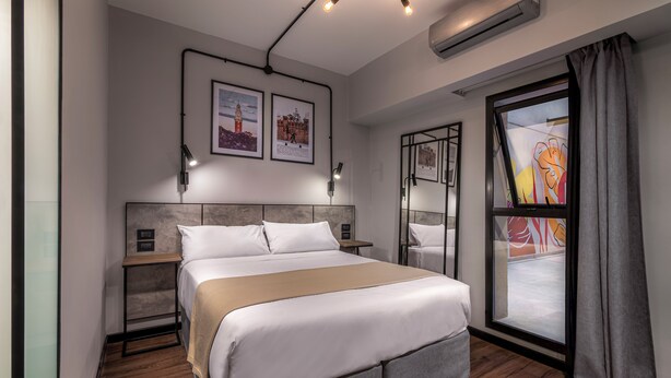 Una habitación de hotel moderna con una cama grande, mesitas de noche, una ventana con vistas y obras de arte en las paredes.