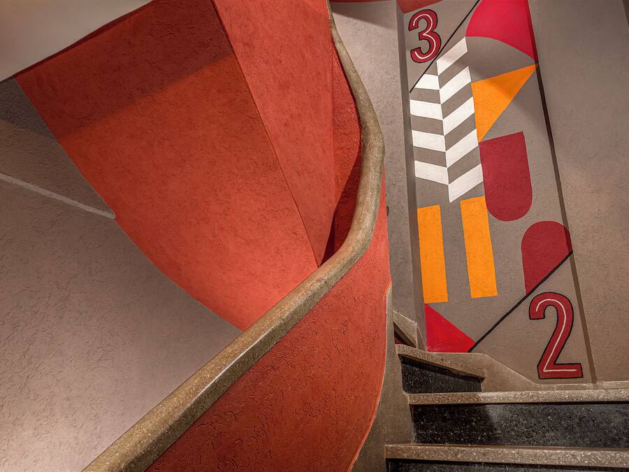 Primer plano de una escalera con alfombra roja y una pared con un diseño geométrico y números.