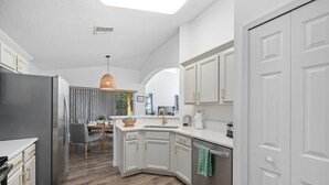 A modern kitchen with white cabinetry, a stainless steel refrigerator, and a dining area with a table and chairs. - 5 Bedroom Spacious Home with Private Pool and Resort Pool in Terra Verde Resort (Kissimmee)