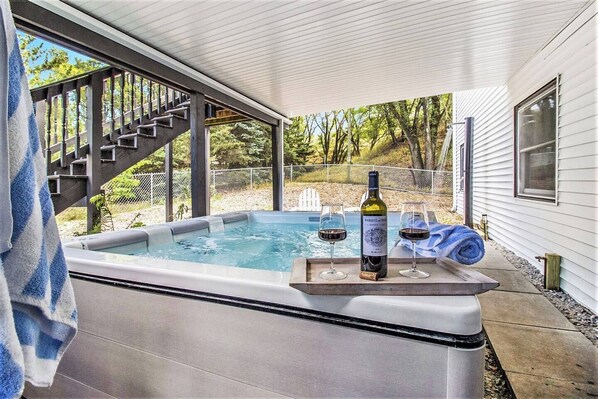 A hot tub with a wooden bench, two glasses of wine, and a bottle of wine.