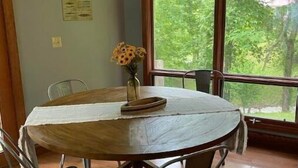 A dining area with a round table, four chairs, a chandelier, and a large window with a view of trees. - Creekside a piece of heaven (Gallipolis)