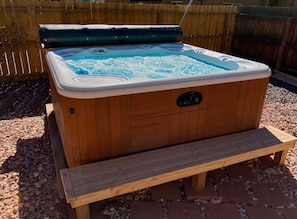 A wooden hot tub with a bench in front, surrounded by gravel and a wooden fence.