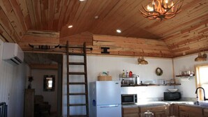A rustic kitchen with wooden beams, a refrigerator, a microwave, and a chandelier.