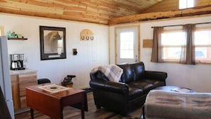 A cozy room with a wooden ceiling, a black leather sofa, a small table, and a window with curtains.