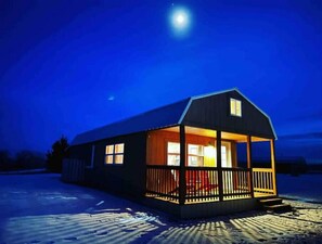 A single-story cabin with a porch, large windows, and a visible door. - Hayfield Cabin 1, a place to get away from it all!
 (Fort Laramie)