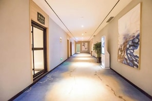 A hotel corridor with a carpeted floor, a door on the left, and a wall-mounted artwork on the right. - Huifeng Hotel (Longkou)