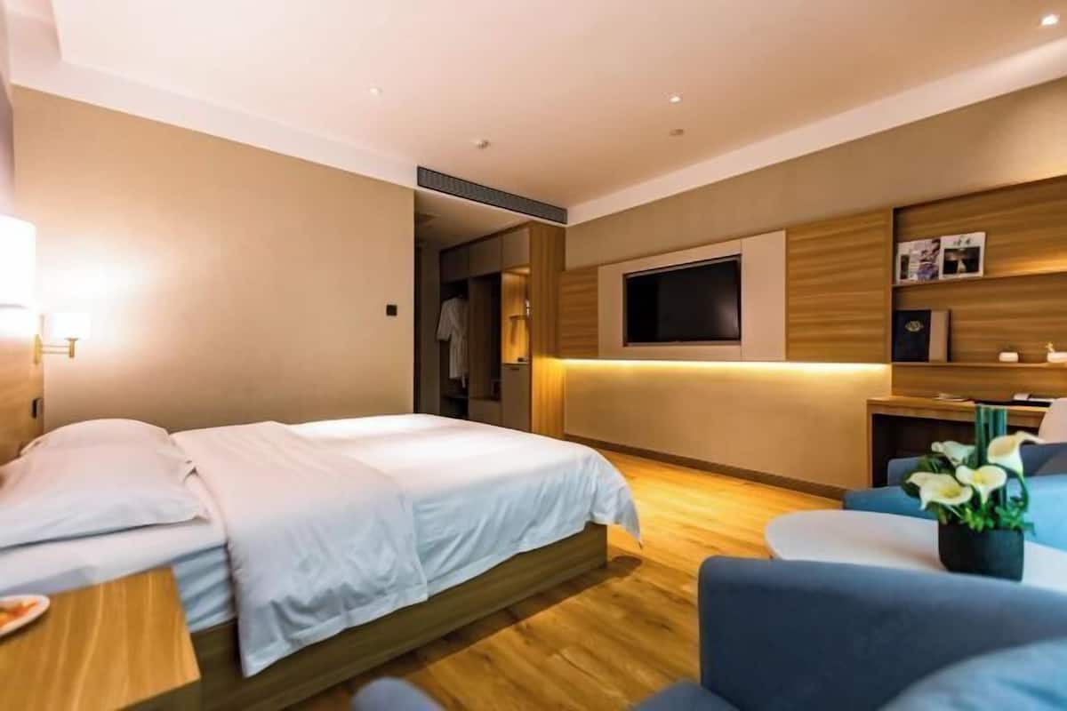 A modern hotel room with a bed, a TV, a seating area, and a small table.