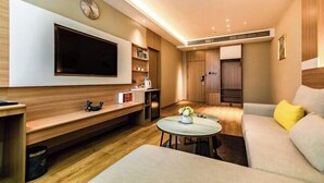 A modern living room with a flat-screen TV mounted on the wall, a sofa, a coffee table, and a dining area with a small table and chairs. - Huifeng Hotel (Longkou)