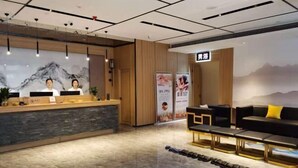 A reception area with a wooden reception desk, two receptionists, a black leather sofa, and a row of black shoes on the floor. - Huifeng Hotel (Longkou)