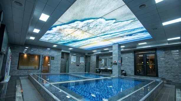 A modern indoor swimming pool with a large ceiling projection, tiled walls, and a clear view of the pool area. - Huifeng Hotel (Longkou)
