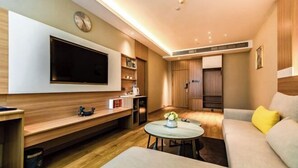 A modern living room with a flat-screen TV, wooden furniture, a round coffee table, and a sofa with a yellow pillow. - Huifeng Hotel (Longkou)