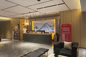 Een hotel receptie met een receptiebalie, een wachtruimte met een bank en een zitbank, en een grote poster aan de muur.