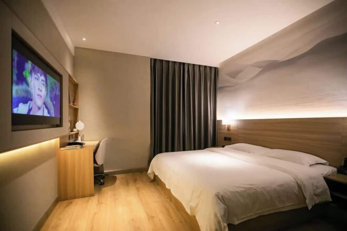 A hotel room with a bed, a desk with a chair, a television, and a large window with curtains.