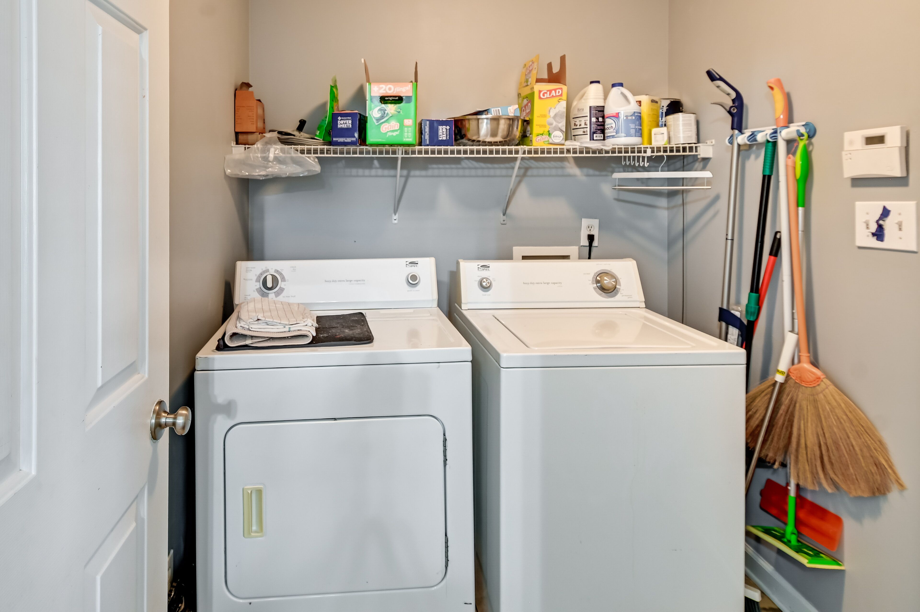 A laundry area with two washing machines, a shelf with cleaning supplies, and a broom.