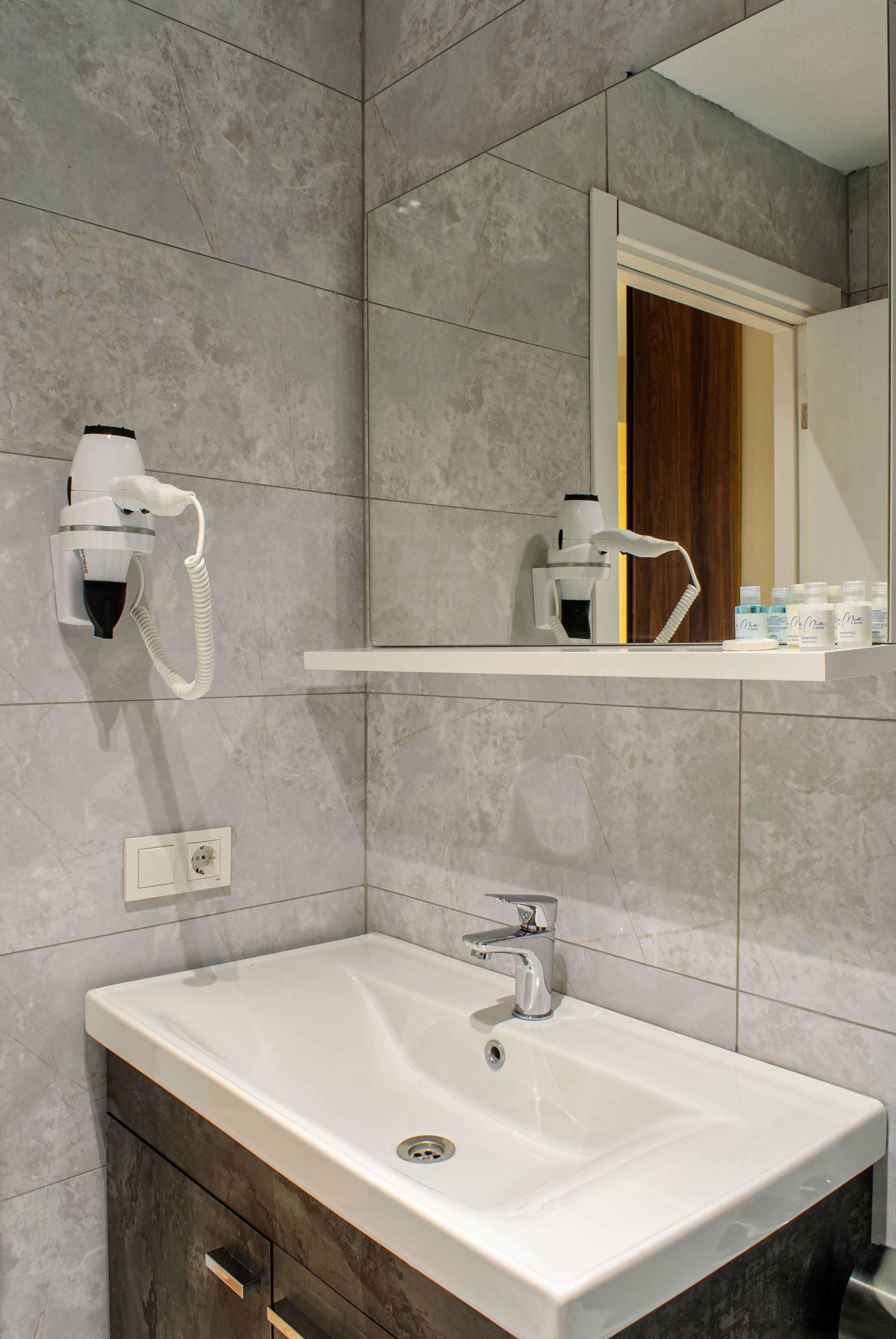 Un bagno moderno con un lavandino bianco, un asciugacapelli e uno specchio sopra al lavandino.