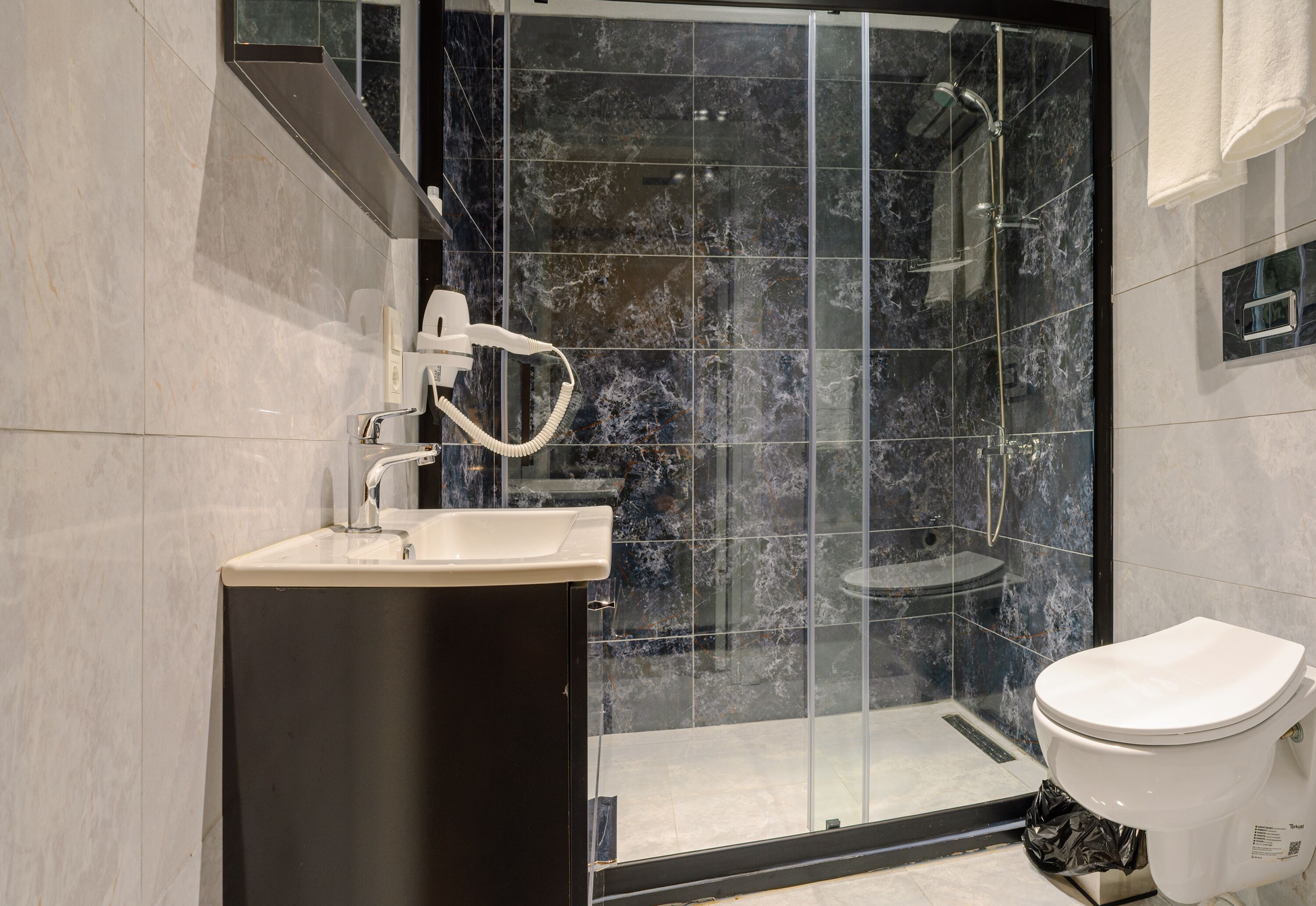 Un baño moderno con ducha envuelta en vidrio, inodoro blanco y lavamanos con mueble negro.