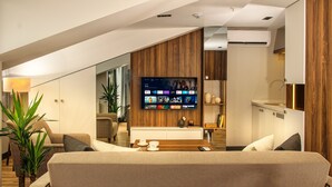 Una habitación de hotel moderna con una televisión de pantalla plana grande montada en la pared, un sofá, una mesita de centro y una planta en maceta.