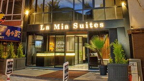Un hotel llamado "La Mia Suites" con una fachada moderna, ventanas grandes y una entrada acogedora.