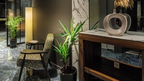 Un vestíbulo moderno con una recepción de mármol, una planta en maceta, una silla y un espejo grande que refleja la decoración.