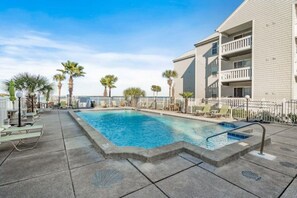 A swimming pool with lounge chairs and palm trees, surrounded by a building with balconies. - Okaloosa's Islander on the Bay (Fort Walton Beach)