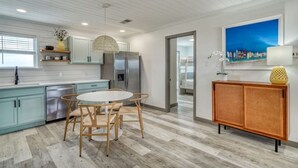 Une cuisine moderne avec des meubles de couleur bleu clair, un réfrigérateur en acier inoxydable, une table de salle à manger ronde avec des chaises et un buffet en osier.