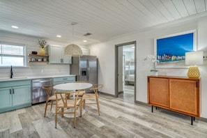 A modern kitchen with light blue cabinets, a stainless steel refrigerator, a round dining table with chairs, and a wicker sideboard. - Okaloosa's Islander on the Bay (Fort Walton Beach)