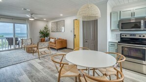 Une cuisine moderne équipée d’appareils électroménagers en acier inoxydable, un coin repas avec une table ronde et des chaises, et une vue sur l’océan grâce à de grandes fenêtres.