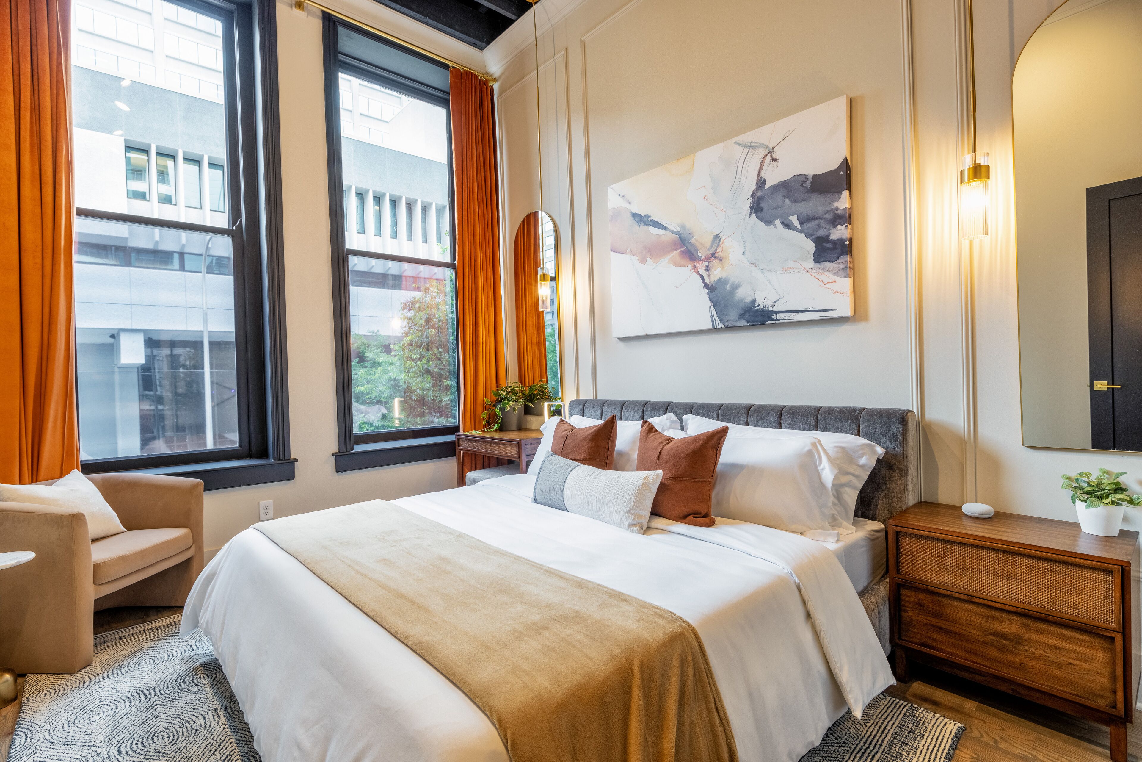 Een moderne hotelkamer met een groot bed, een stoel, een nachtkastje met lamp en een groot raam met gordijnen.