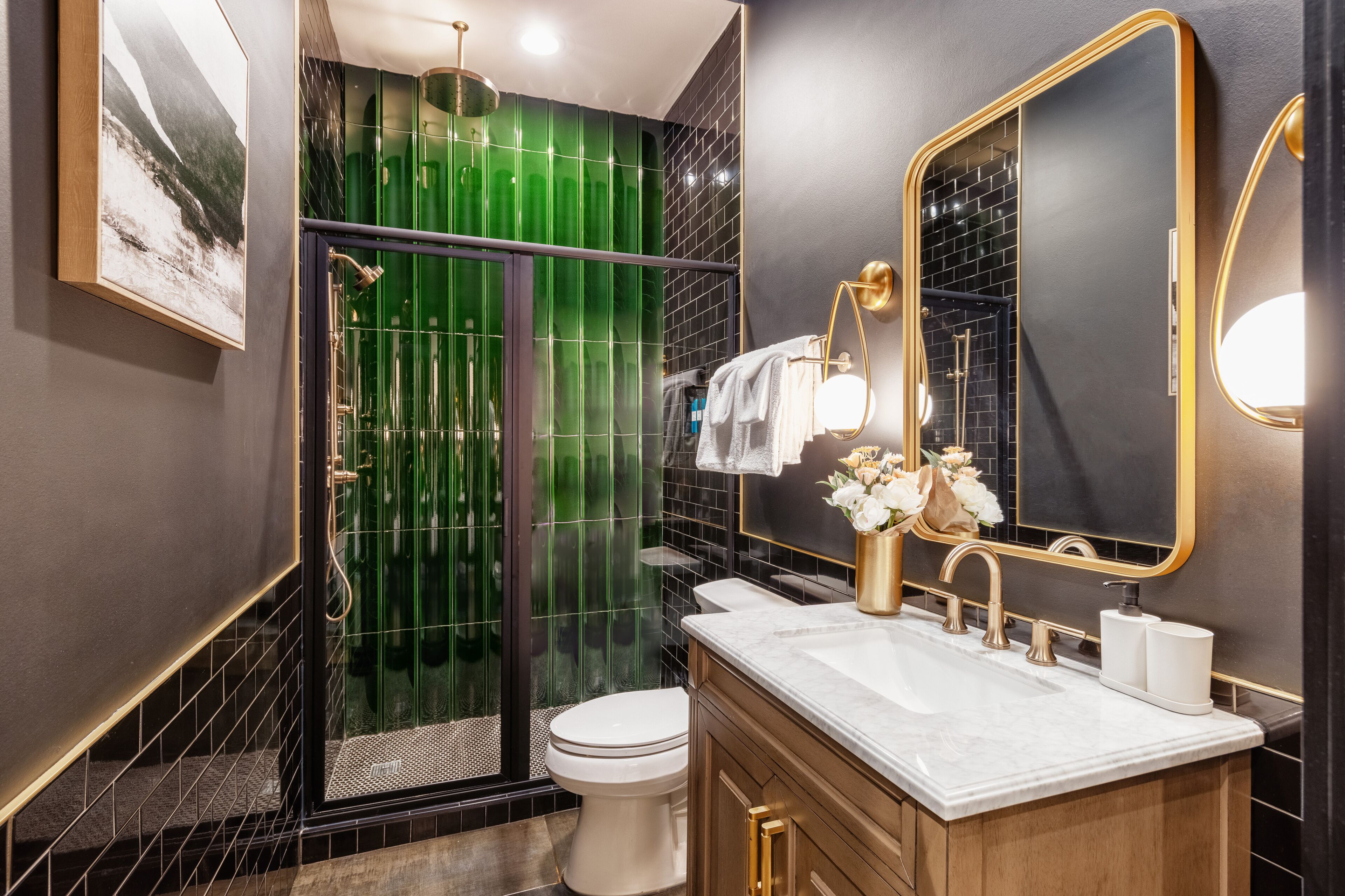 A modern bathroom with a glass-enclosed shower, a white toilet, and a vanity with a gold faucet.
