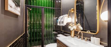 Un baño moderno con ducha envuelta en vidrio, inodoro blanco y tocador con grifo dorado.