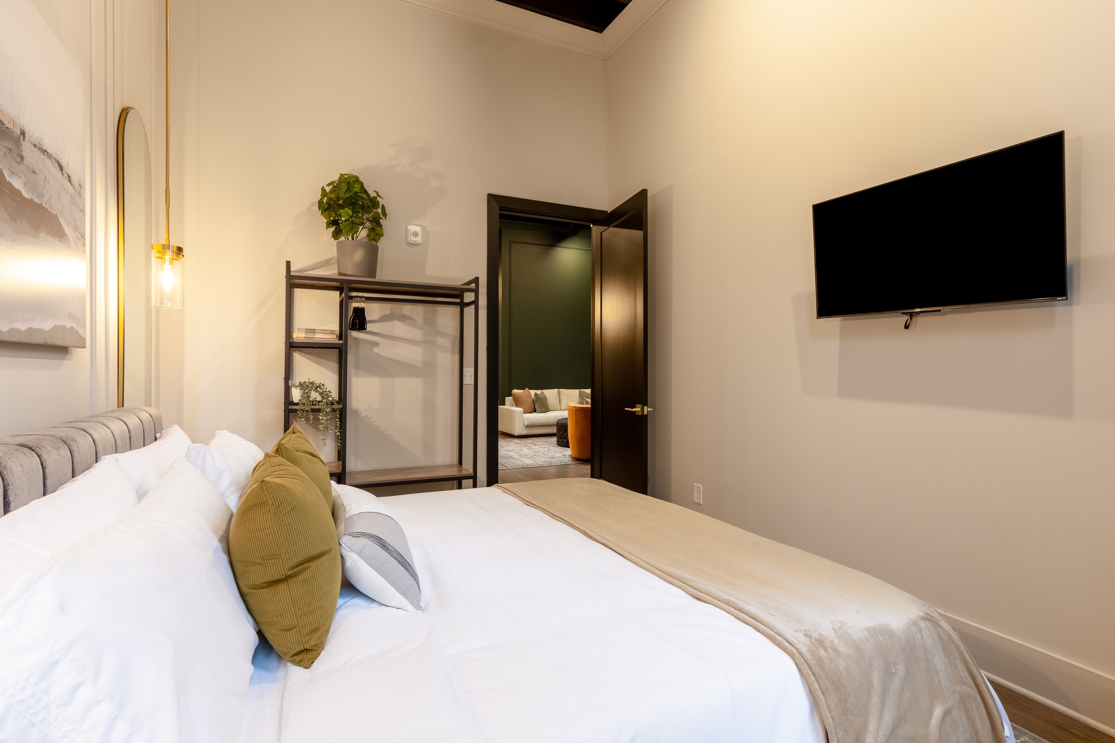 Ein modernes Schlafzimmer mit einem Bett, einem an der Wand montierten Fernseher und einer Tür zu einem anderen Raum.