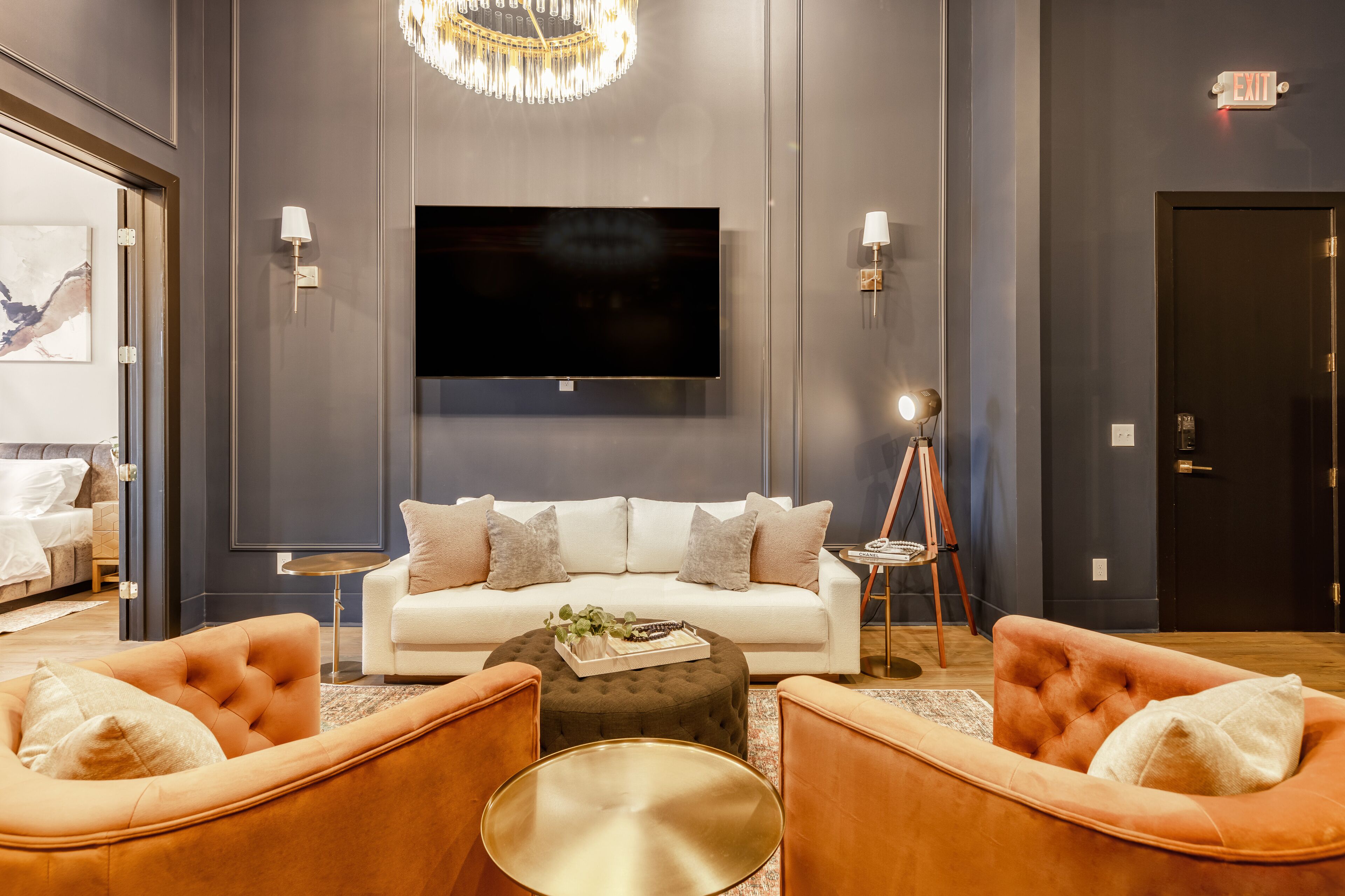 A modern living room with a large flat-screen TV, a white sofa, and two orange armchairs.