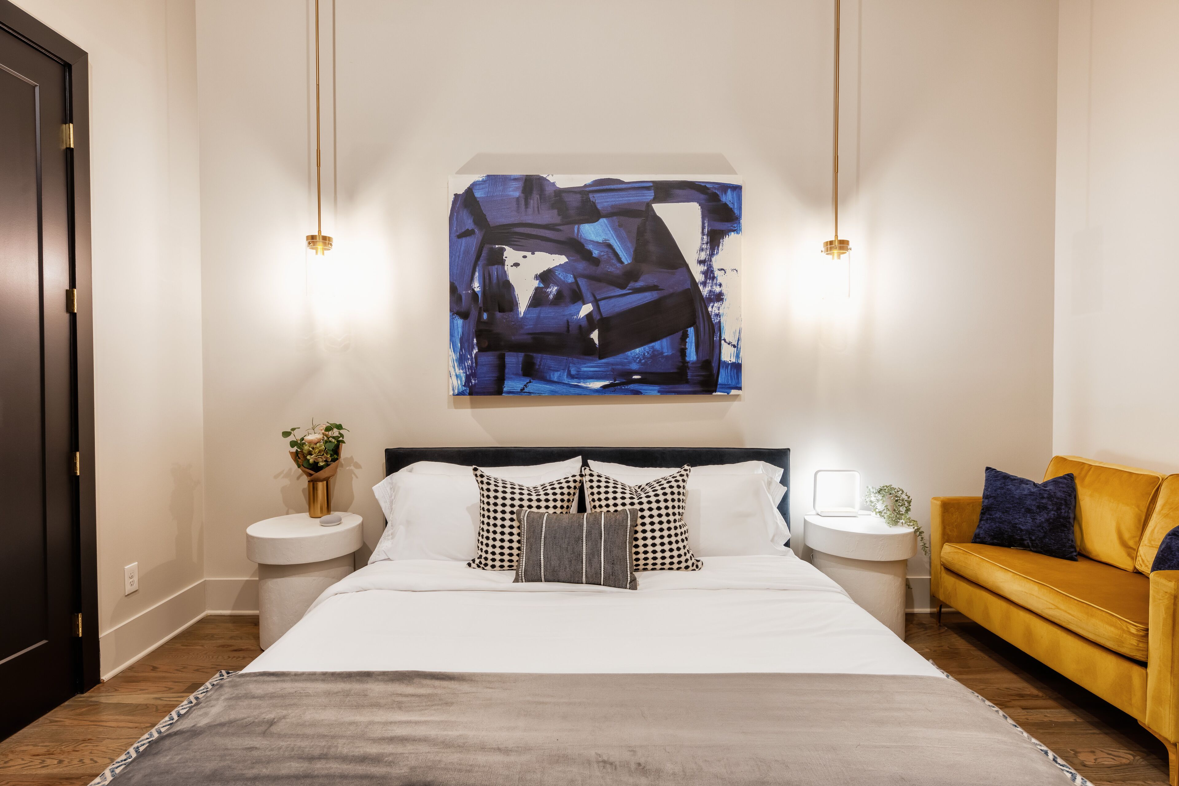 Une chambre moderne avec un grand lit, des tables de chevet, un canapé et un tableau abstrait accroché au mur.