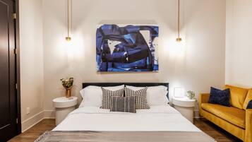 Une chambre moderne avec un grand lit, des tables de chevet, un canapé et un tableau abstrait accroché au mur.