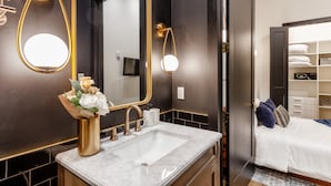 A modern bathroom with a gold-framed mirror, a white sink, and a vase of flowers. - Union Street Lofts (Nashville)