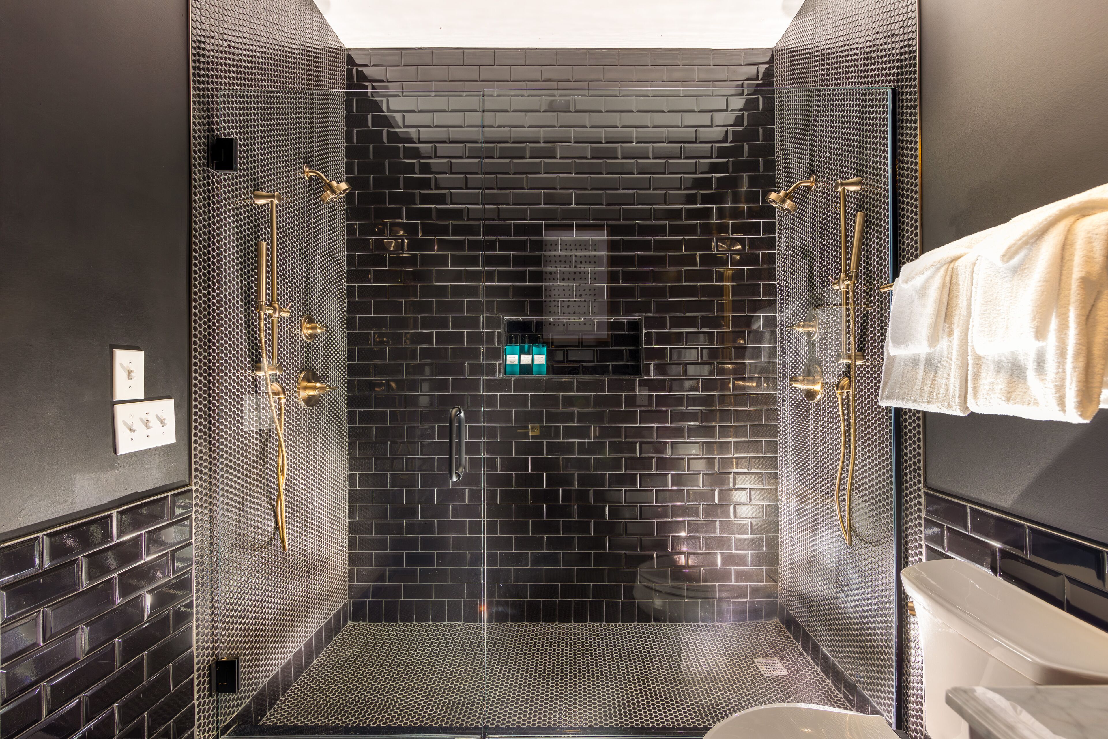 A modern shower area with a black tiled wall, a glass door, and a white bathtub.