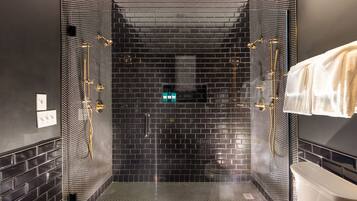 A modern shower area with a black tiled wall, a glass door, and a white bathtub.