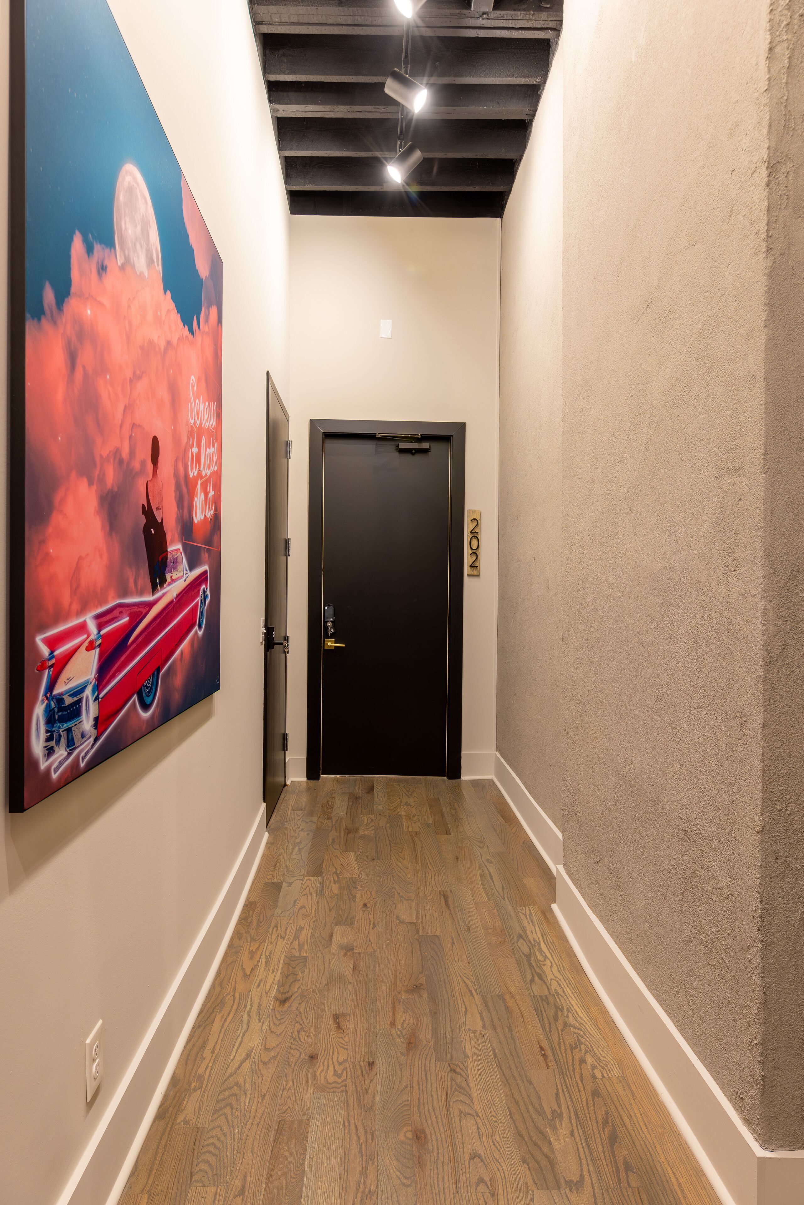 A hallway with a wooden floor, a black door, and a large poster on the wall.