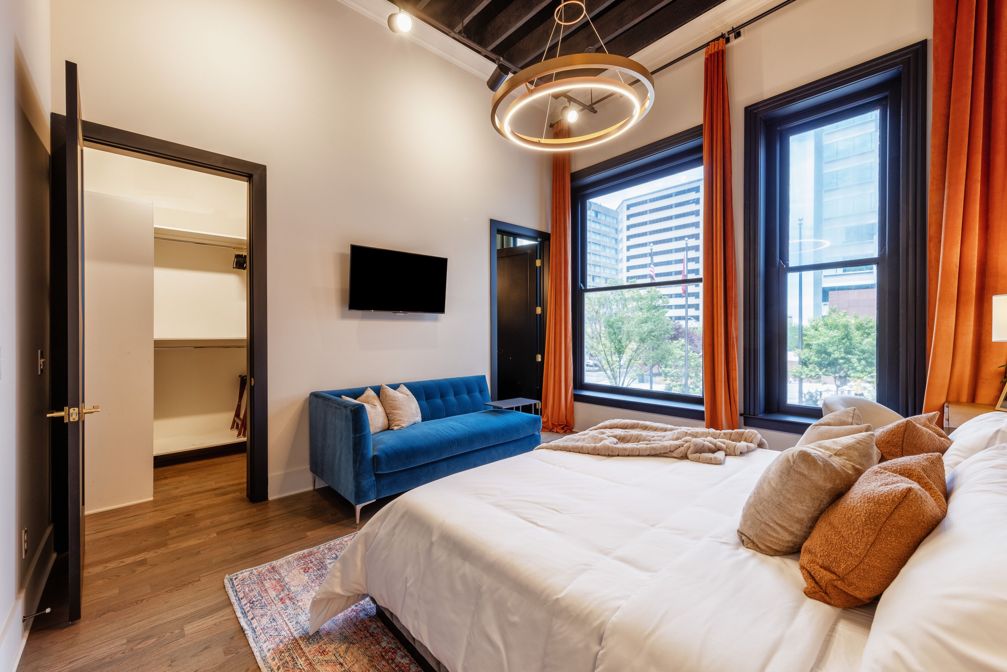 Een moderne slaapkamer met een groot bed, een blauwe bank, een televisie en uitzicht op de stad.