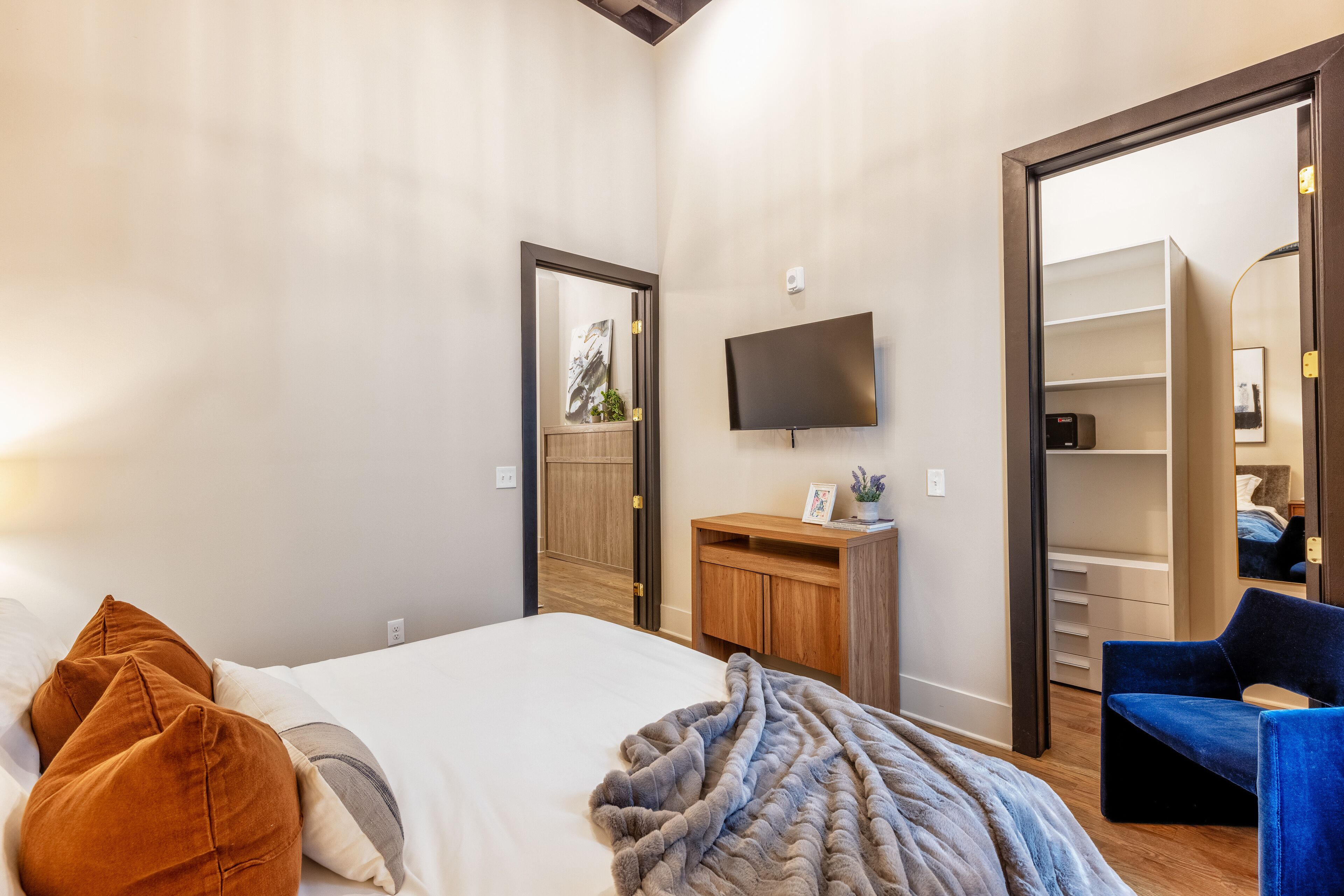 Um quarto com cama, televisão, escrivaninha de madeira e guarda-roupa.