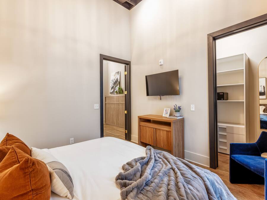 Um quarto com cama, televisão, escrivaninha de madeira e guarda-roupa.