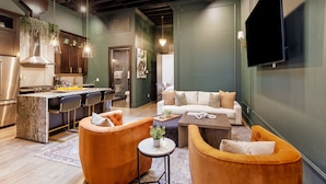 A modern kitchen with a bar area, a living room with a sofa and chairs, and a flat-screen TV mounted on the wall. - Union Street Lofts (Nashville)